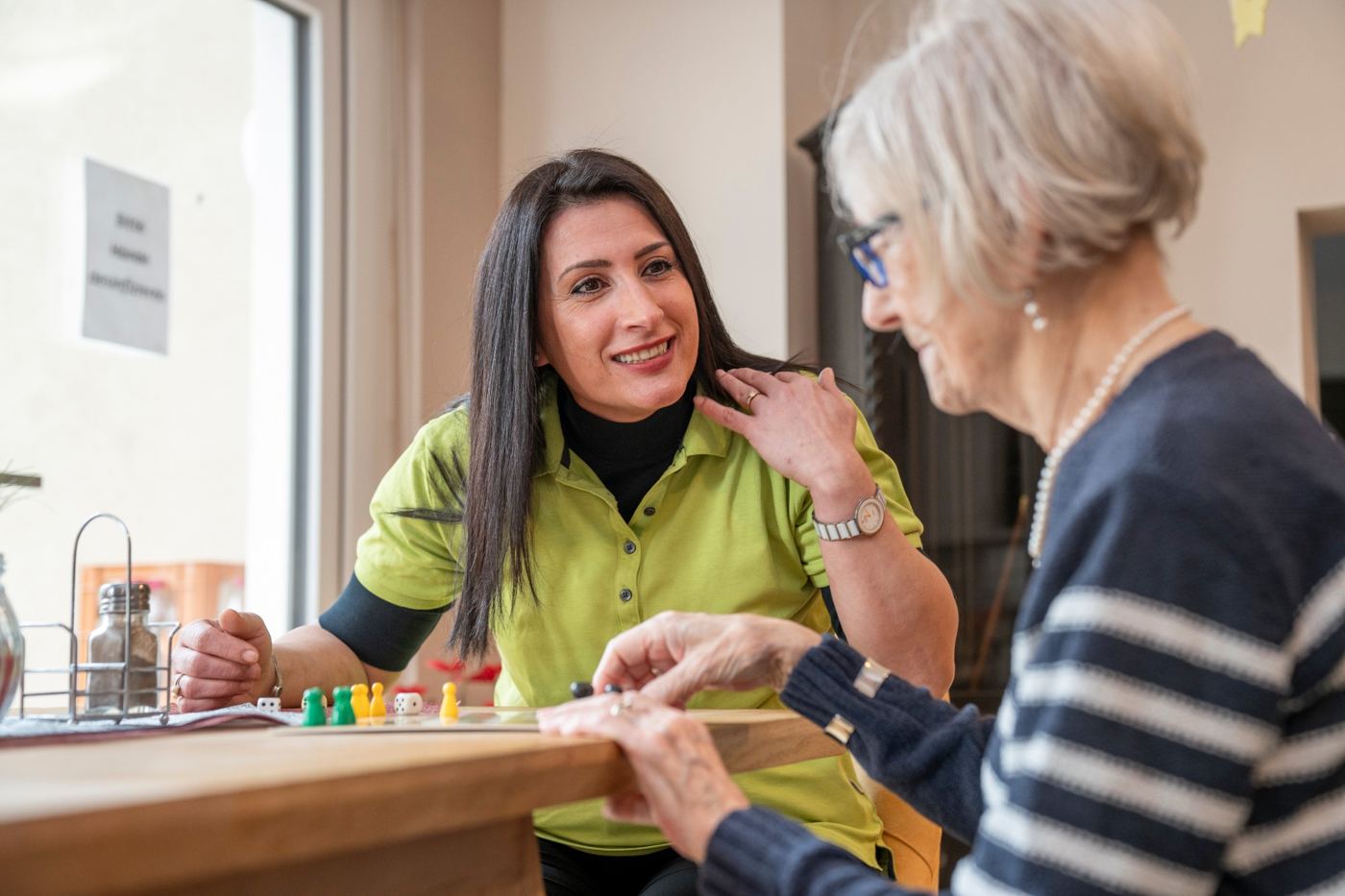 Eine Betreuungskraft und ein Tagesgast lachen gemeinsam am Spieltisch